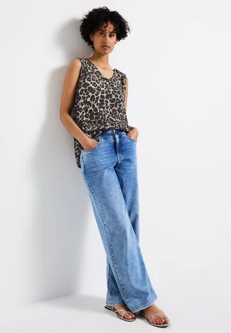 Frau mit Leoparden-Top und weitem Jeans steht lässig an der Wand.